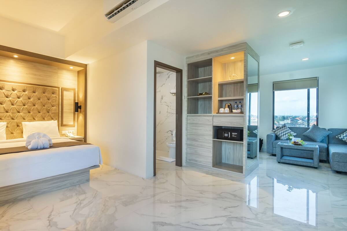Ein modernes Hotelzimmer mit einem großen Bett, einem integrierten Kleiderschrank, einer Sitzecke mit einer Couch und Blick auf die Stadt.