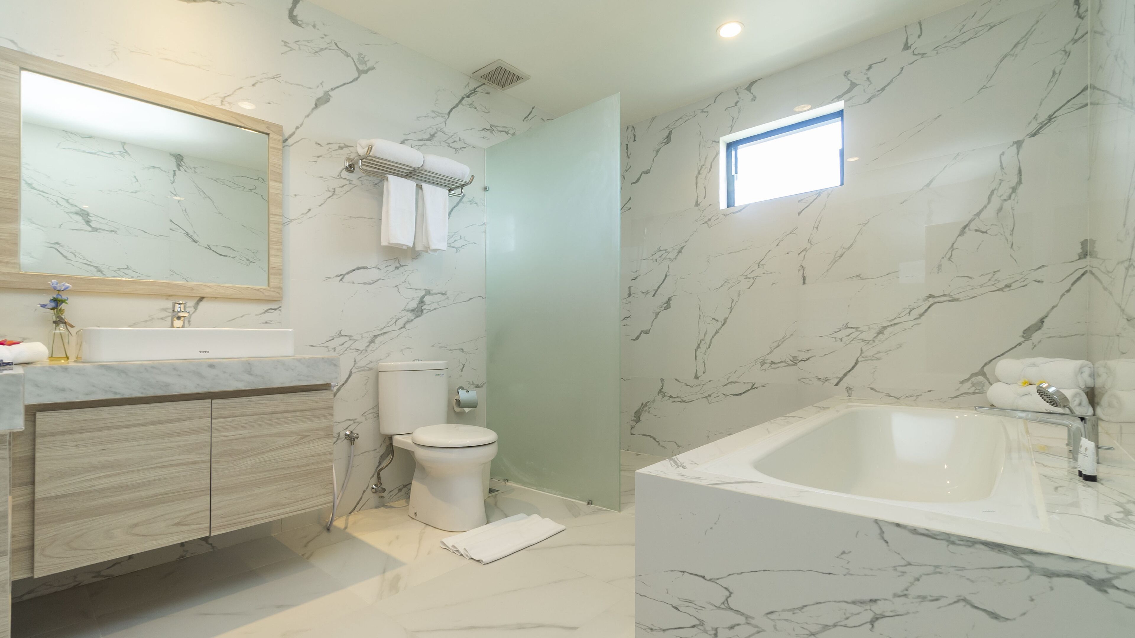A modern bathroom with a marble backsplash, a large bathtub, a toilet, and a vanity with a mirror.