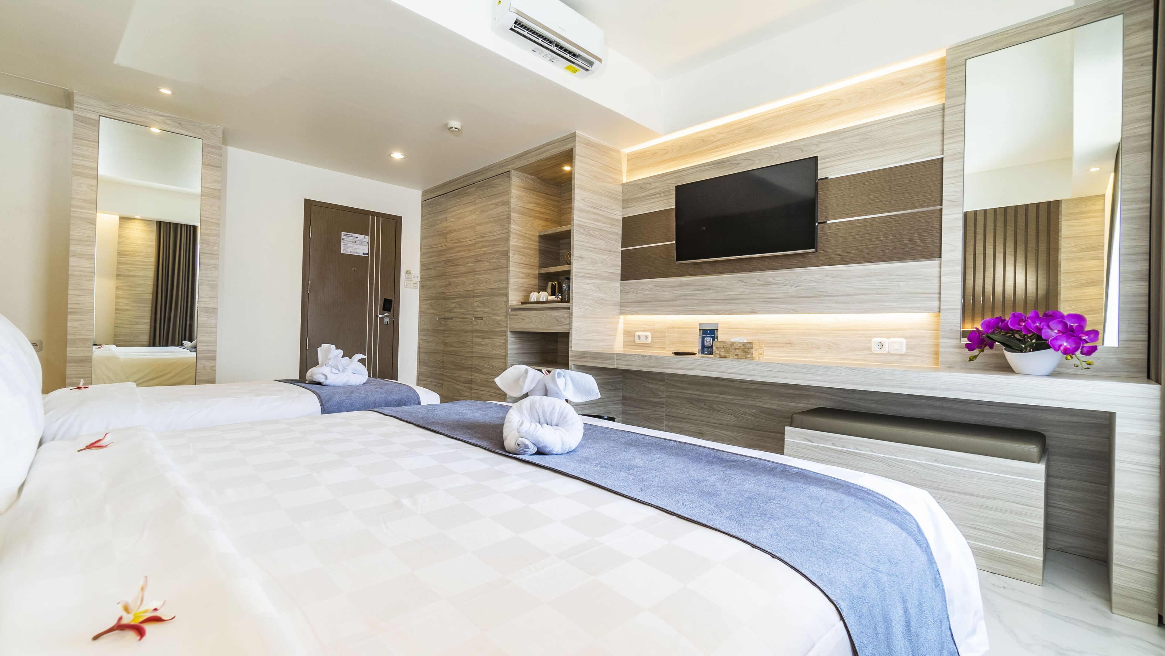 Quarto de hotel com uma cama grande, uma mesa com televisão de tela plana, um espelho e uma orquídea em vaso.