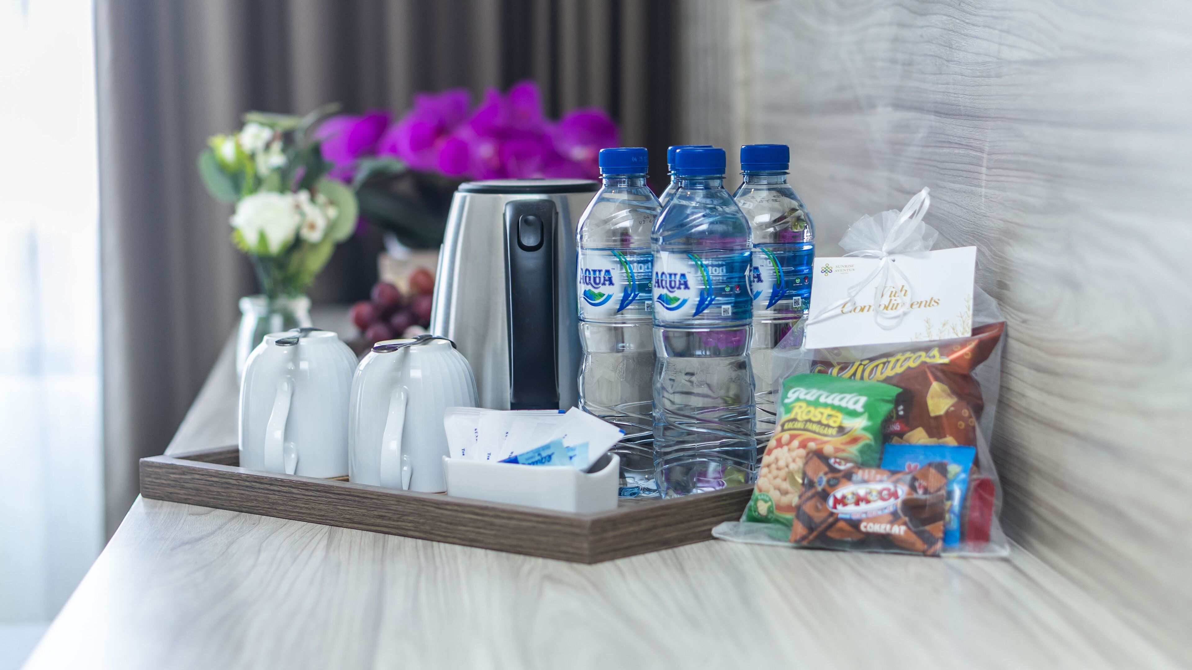 A tray with water bottles, a coffee maker, and a bag of snacks on a hotel room table.