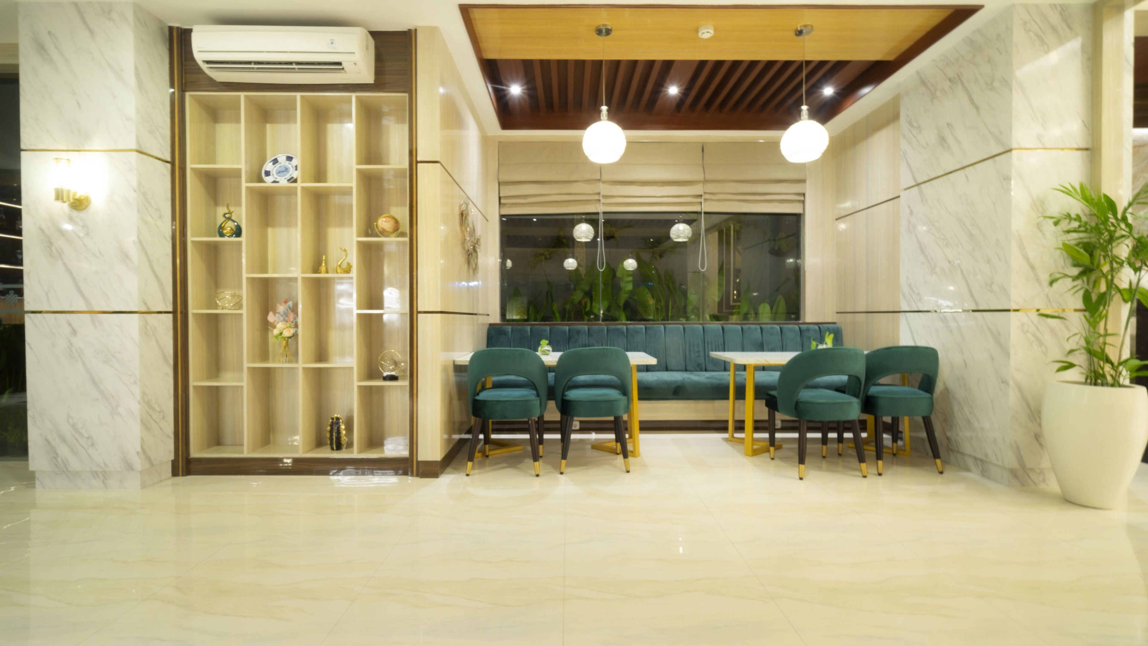 Un interior moderno con suelo de mármol, una estantería empotrada, una zona de estar con sillones tapizados en verde e iluminación colgante.