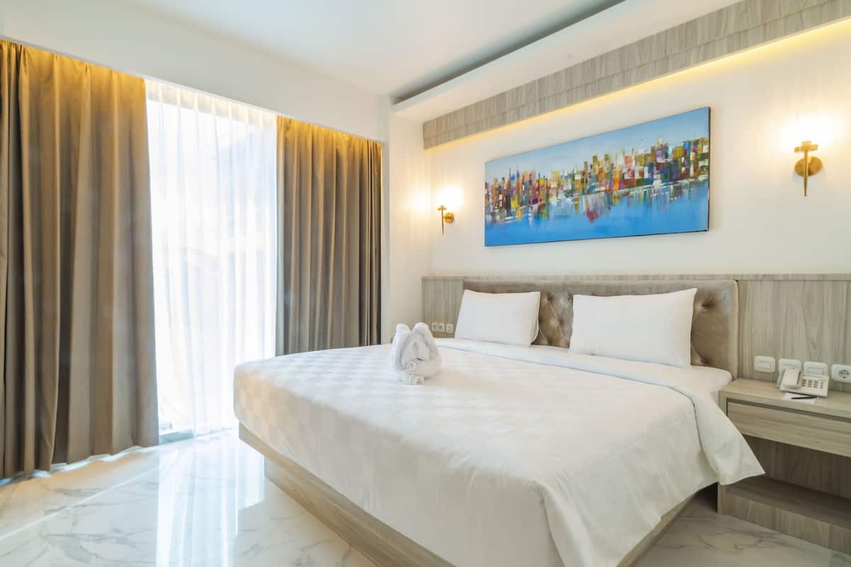 Ein Hotelzimmer mit einem großen Bett, einem Gemälde an der Wand und einem Fenster mit Vorhängen.