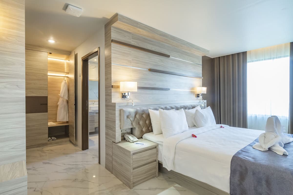 Ein modernes Hotelzimmer mit einem großen Bett, einem Nachttisch mit Telefon, einem Spiegel und einem Badezimmer mit Handtuchhalter.