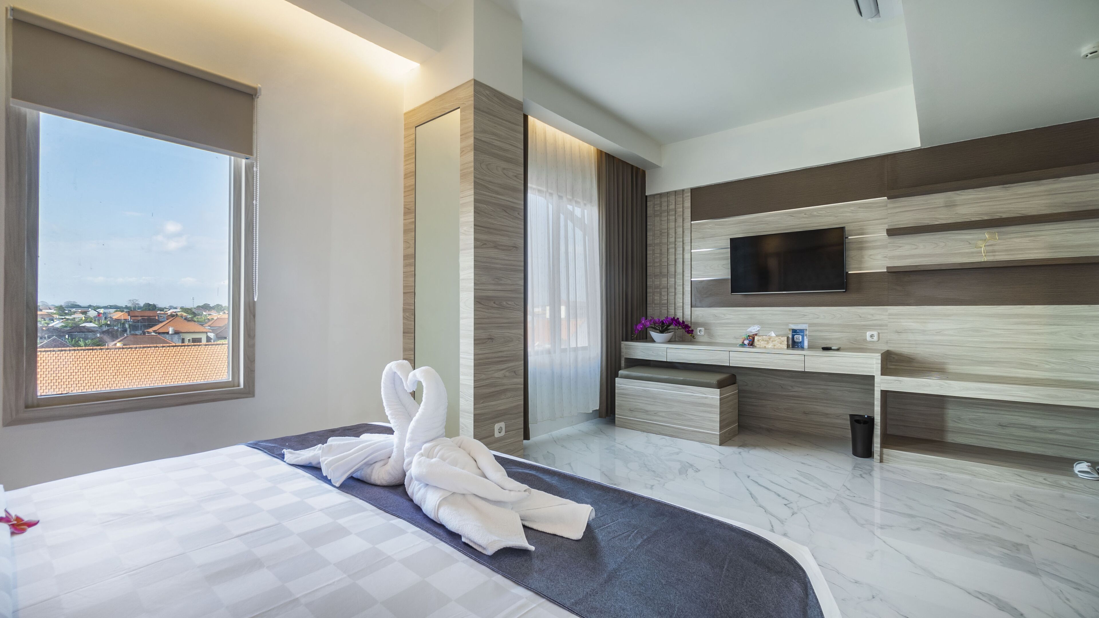 A modern hotel room with a large bed, a TV mounted on the wall, a bathroom with a mirror, and a view of the cityscape.