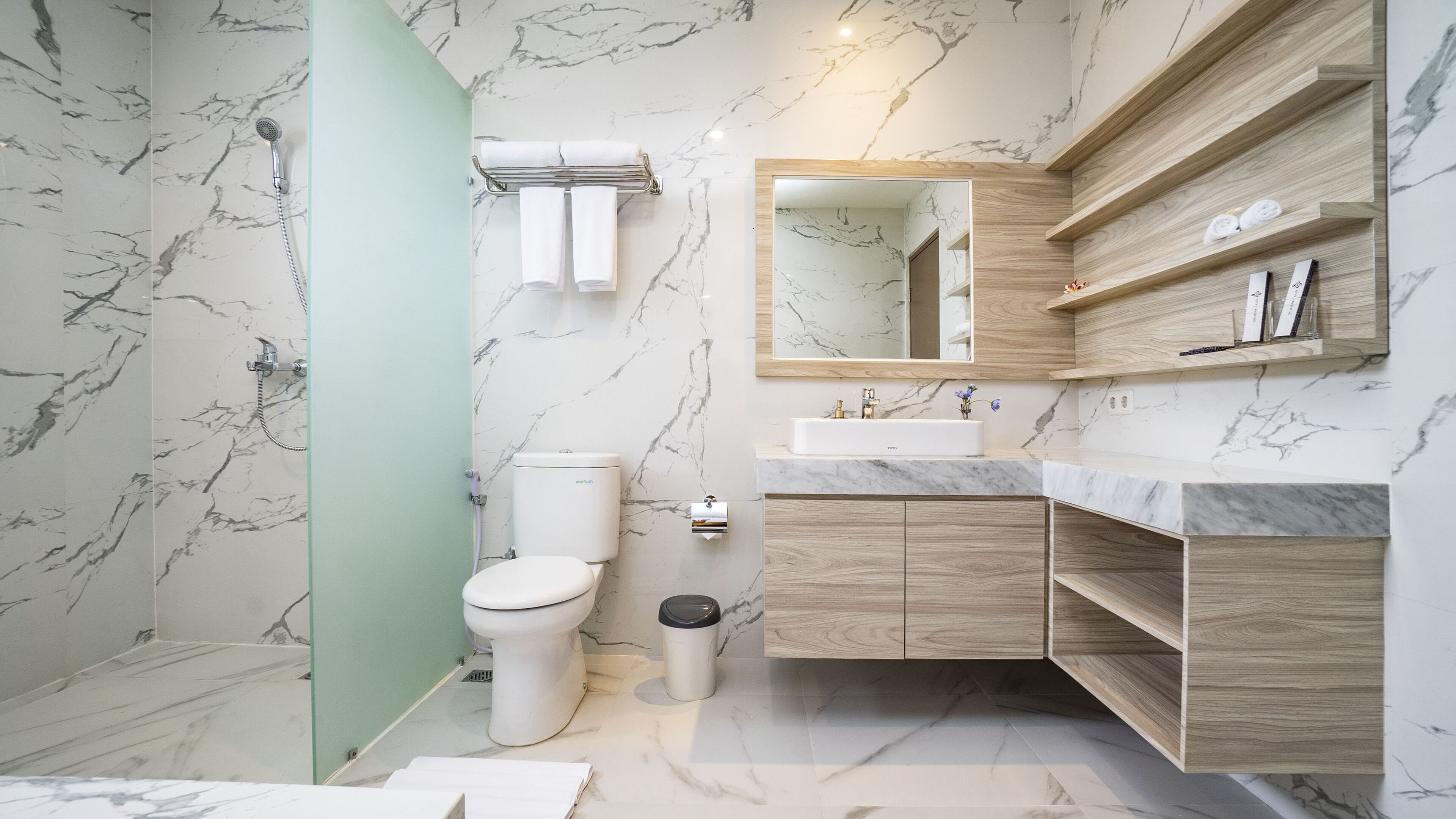 A modern bathroom with a marble wall, a toilet, a sink, and a mirror.
