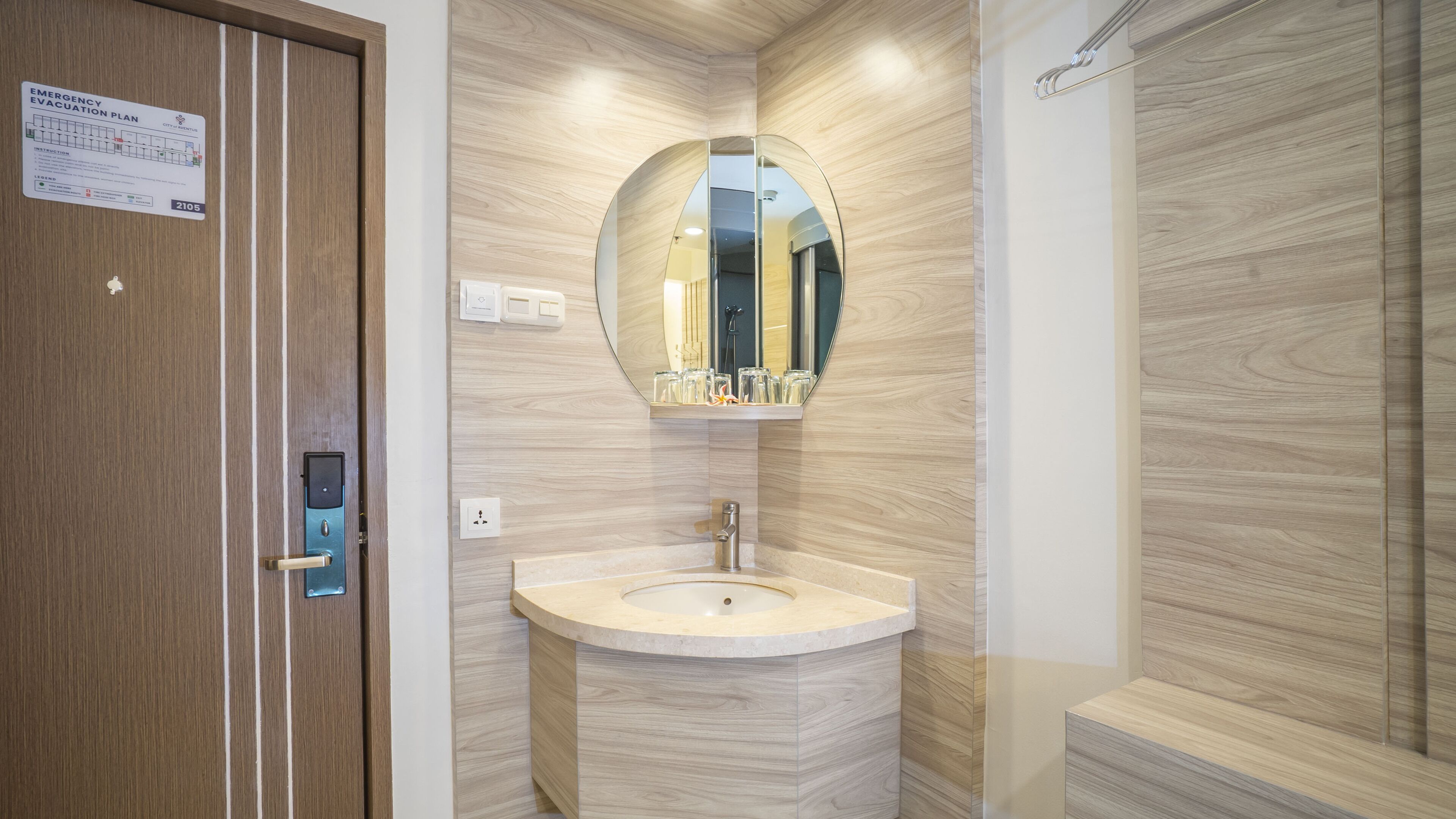Un bany modern amb una porta de fusta, un mirall rodó, un lavabo i una zona de dutxa.