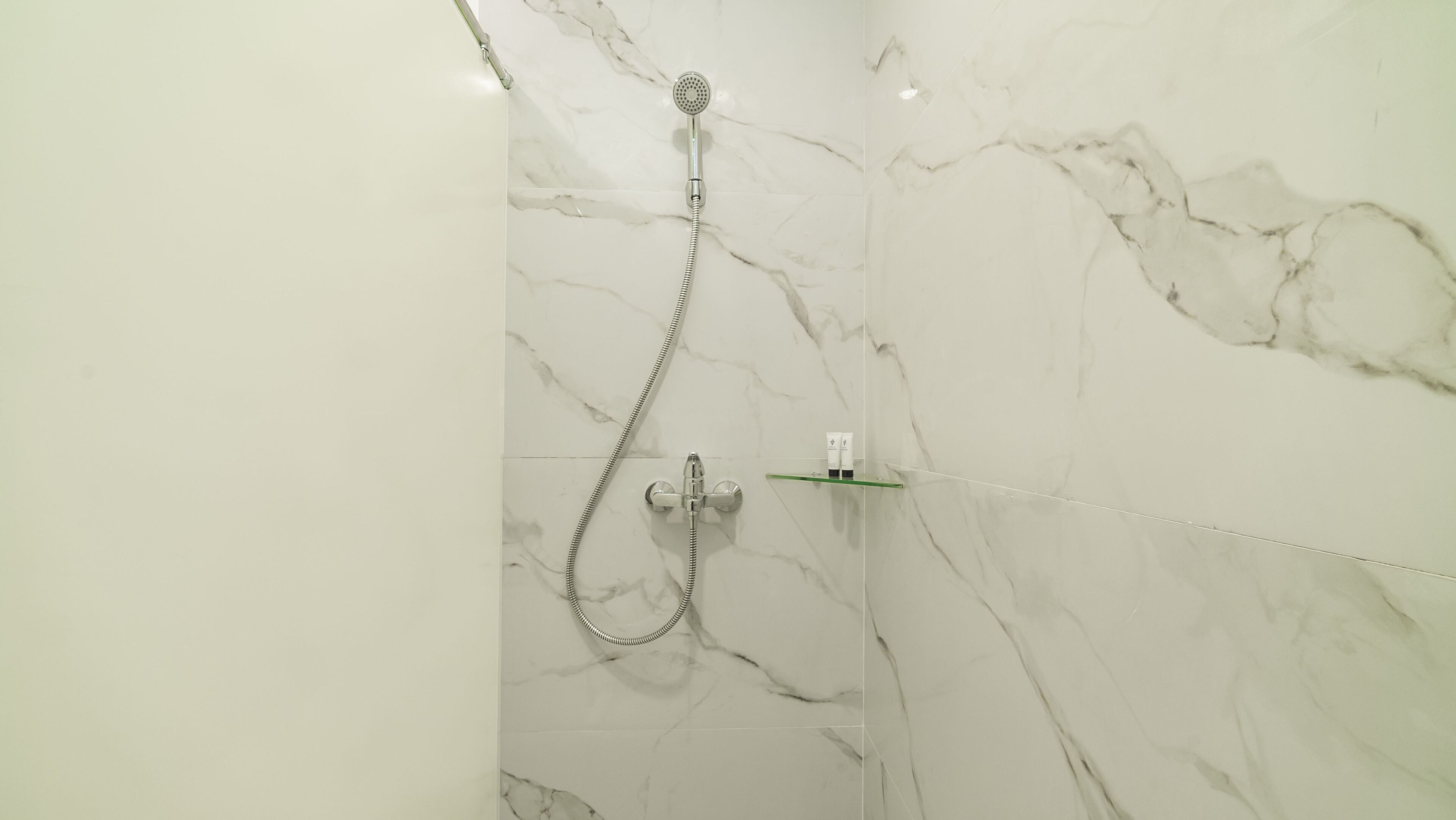A bathroom with a shower, marble walls, and a glass shelf.