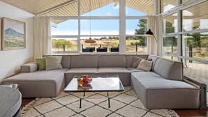 Uma sala de estar moderna com sofá seccional, mesa de centro de vidro e grandes janelas com vista para o exterior.