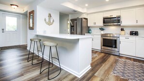 A modern kitchen with white cabinetry, stainless steel appliances, and a central island with bar stools. - Snook Away - Six bedroom bay front home nicely updated (Captiva)