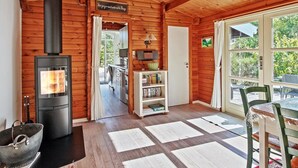Un intérieur de chalet chaleureux avec un poêle à bois, un coin repas avec une table et des chaises, et une cuisine équipée d’appareils modernes.