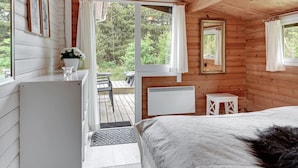 Une cabane avec un intérieur en bois, un lit, une petite table, un miroir et une vue sur l’extérieur.