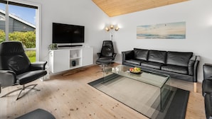 Un soggiorno moderno con soffitto in legno, un'ampia televisione a schermo piatto, un divano in pelle nera e un tavolino da caffè in vetro.