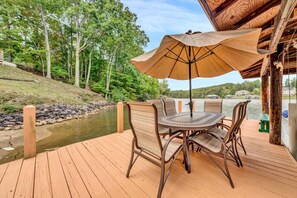 A wooden deck with a table and chairs, an umbrella, and a view of a river and trees. - Dock Days- Deep water and fantastic wide water views. Volley Ball and horseshoe competitions await. (Moneta)