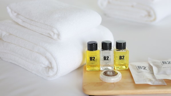 Toallas blancas dobladas con cuidado, tres botellas de champú acondicionador B2, una botella de gel de baño y ducha B2, y un paquete de bastoncillos de algodón B2 sobre una bandeja de madera.