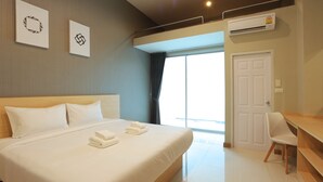 A hotel room with a large bed, a desk, and a chair. There is a window with curtains, an air conditioning unit, and a door. - B2 Suan Luang Rama 9 Srinakarin 42 Boutique & Budget Hotel (Bangkok)