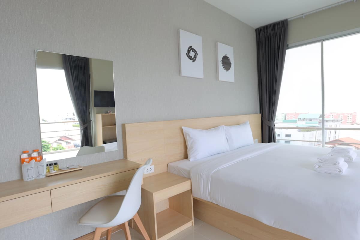 A hotel room with a bed, a desk, a chair, a large window, and two wall art pieces.