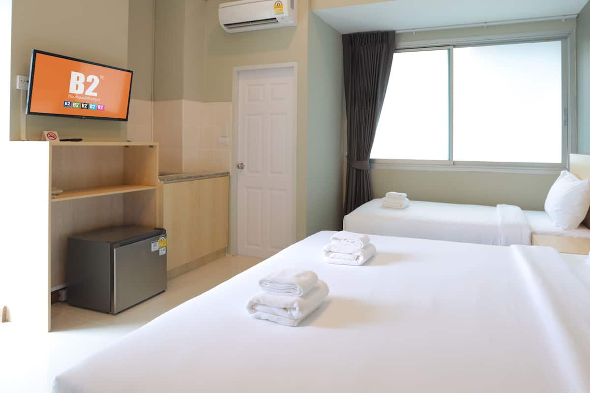 A hotel room with two beds, a television, a wardrobe, and a window with curtains.