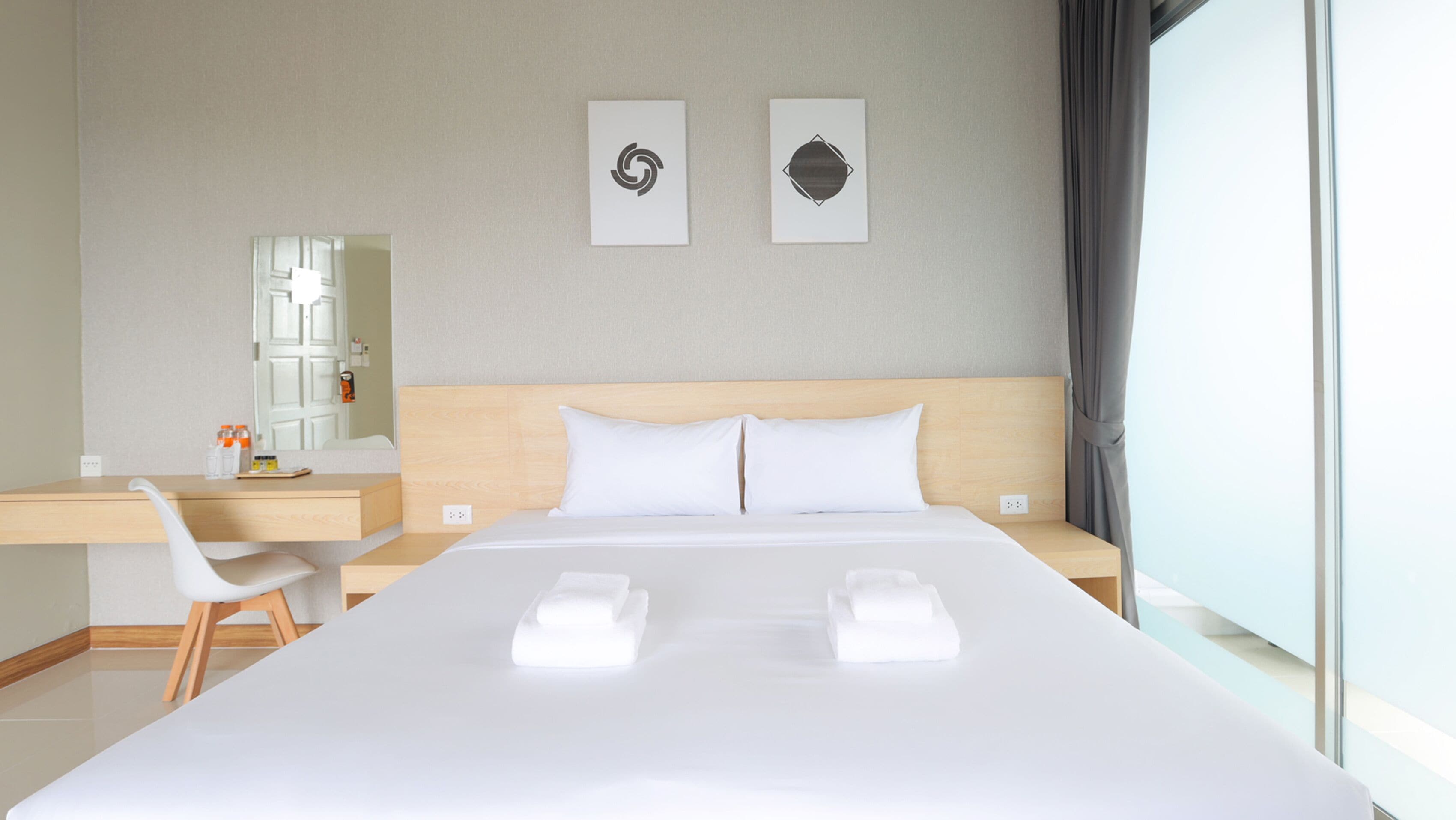 A hotel room with a large bed, a desk, a chair, a mirror, and two wall art pieces.