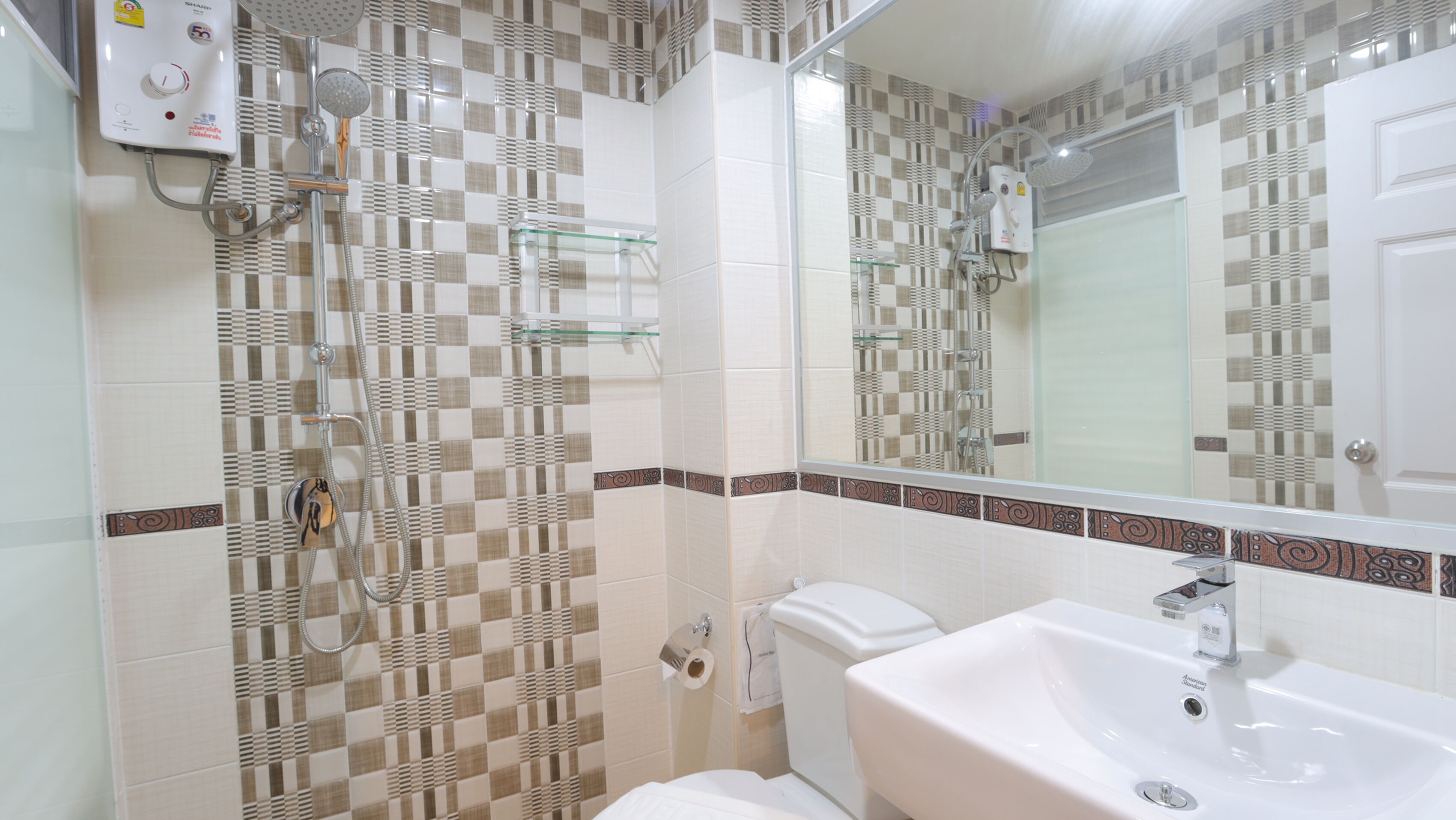 Un baño con pared de baldosas a cuadros, un lavamanos blanco, un inodoro y una ducha con cabezal de ducha de mano.