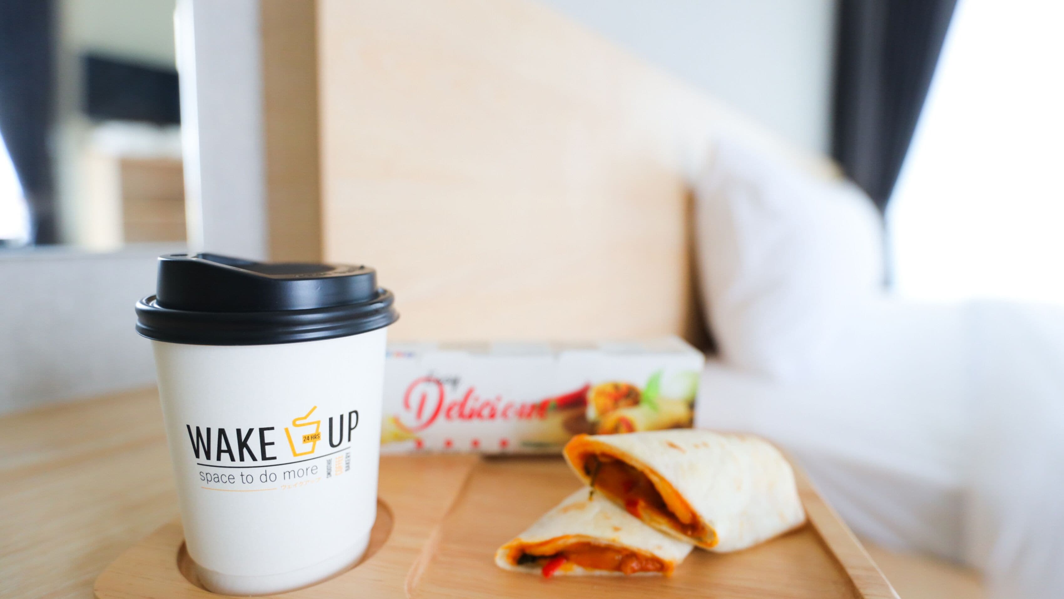 En kop kaffe til takeaway med låg og en burrito på en træbakke.