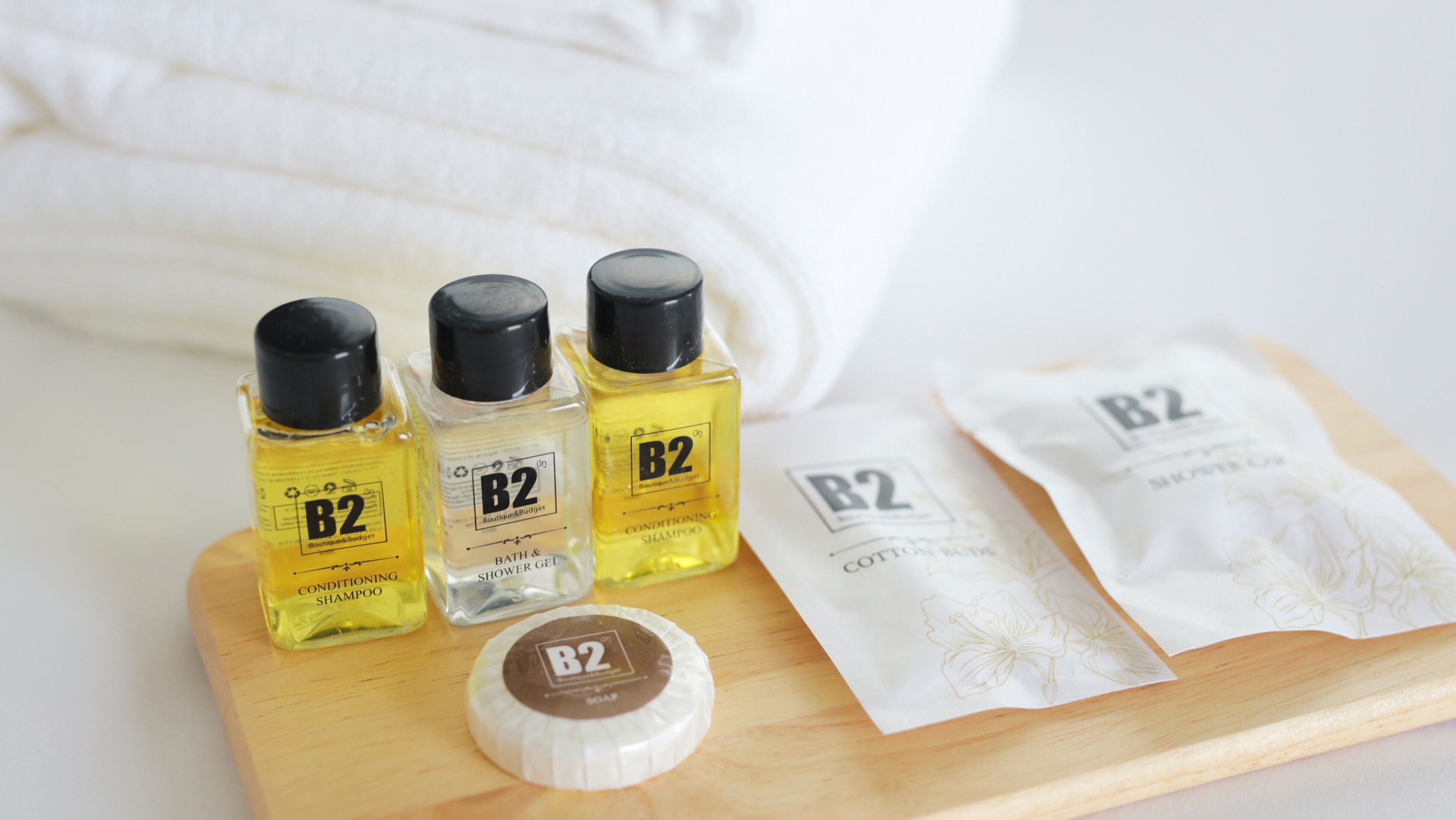 Three bottles of B2 conditioning shampoo, a bottle of B2 conditioning shower gel, and two B2 cotton buds on a wooden tray.