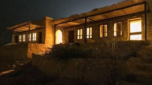 A stone building with multiple windows and a covered entrance, situated on a rocky hillside. - Matan Rural Lodge (At-Tafilah)