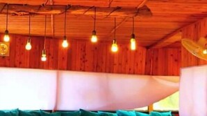 A wooden interior with a sofa and cushions, a ceiling fan, and hanging light bulbs. - Matan Rural Lodge (At-Tafilah)