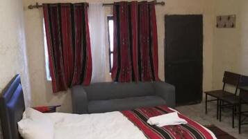 Ein Schlafzimmer mit Bett, einer Couch, einem Schreibtisch und einem Stuhl. Es gibt ein Fenster mit Vorhängen, eine Klimaanlage und eine Deckenleuchte.