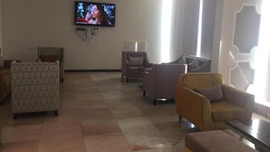 A spacious lobby with a flat-screen TV mounted on the wall, several sofas, and a patterned ottoman. - Kol Alayam Hotel (Makkah)