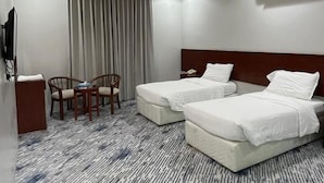 A hotel room with two beds, a desk with a chair, a TV, and an air conditioning unit. - Kol Alayam Hotel (Makkah)