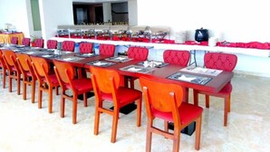 A long dining table with red upholstered chairs, a buffet setup, and a kitchen area in the background. - Kol Alayam Hotel (Makkah)