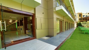 Un edificio moderno con entrada de vidrio, una escalera y una zona de estar exterior cubierta con sillas verdes.