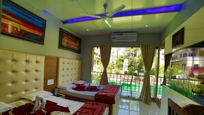 Habitación de hotel con dos camas, ventilador de techo, equipo de aire acondicionado y balcón con vistas al exterior.