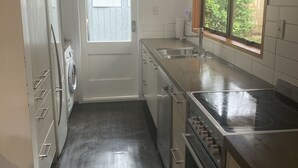 A compact kitchen with a refrigerator, oven, sink, and a window with a view of greenery.