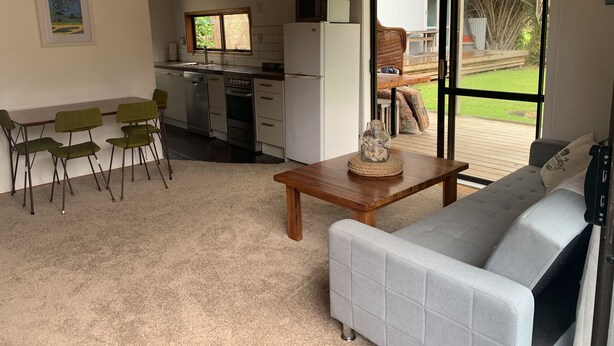 A compact living space with a kitchenette, a dining area with chairs, a sofa, and a large sliding glass door leading to an outdoor deck.