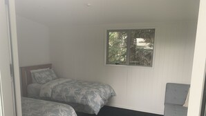 A bedroom with two beds, a window, and a grey sofa.