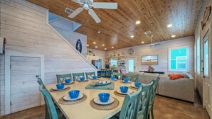 A dining area with a wooden table set for six, surrounded by teal chairs. A staircase leads to an upper level. - Pool Cabana, Backyard w/ Fire Pit, Walk to the Beach | Villa Reel by AvantStay (Port Aransas)