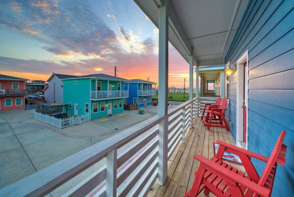 A beachfront property with a wooden deck, red chairs, and a view of colorful buildings and the sunset.