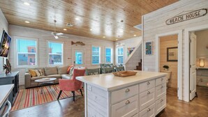A spacious living area with a large island, a sofa, and a dining table. - Pool Cabana, Backyard w/ Fire Pit, Walk to the Beach | Villa Reel by AvantStay (Port Aransas)