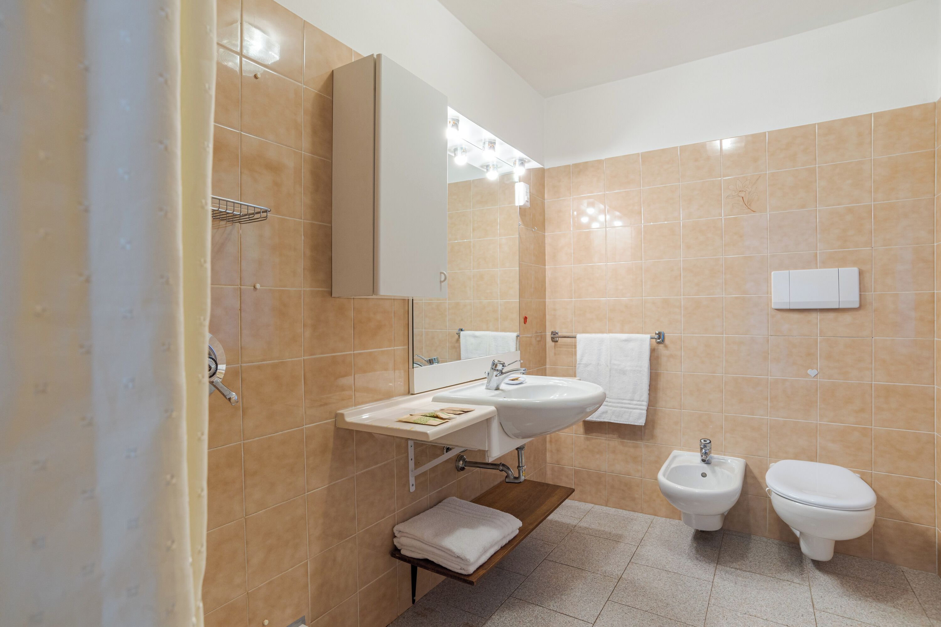 A bathroom with a sink, mirror, towel rack, bidet, and a shelf with folded towels.