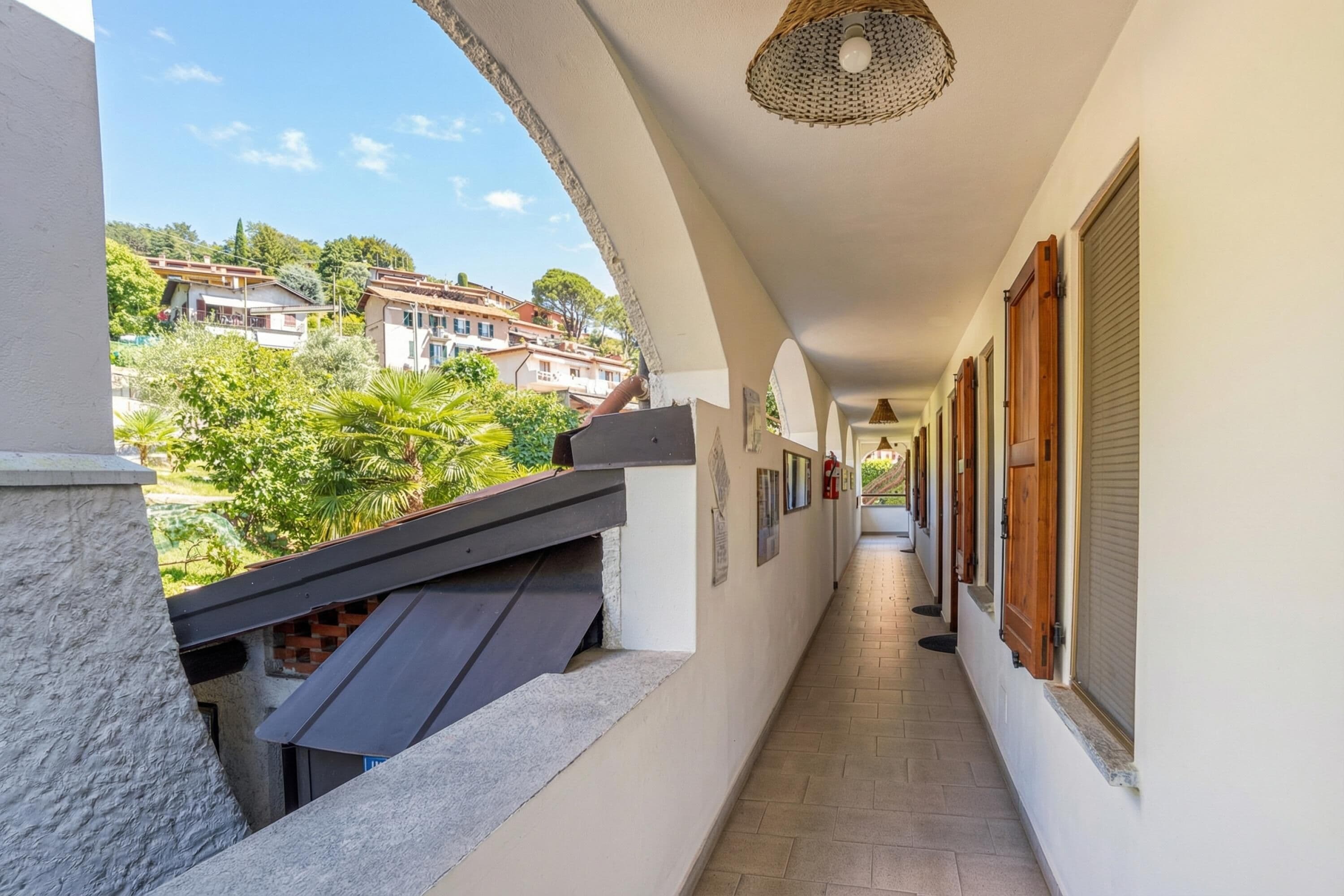 A corridor with a view of houses, a balcony, and a hanging light fixture.