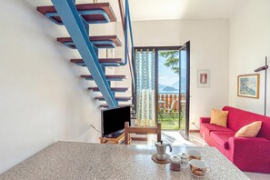 A modern living room with a red sofa, a TV on a stand, a coffee table with cups, and a staircase. - Co.ri. Apartments (Menaggio)