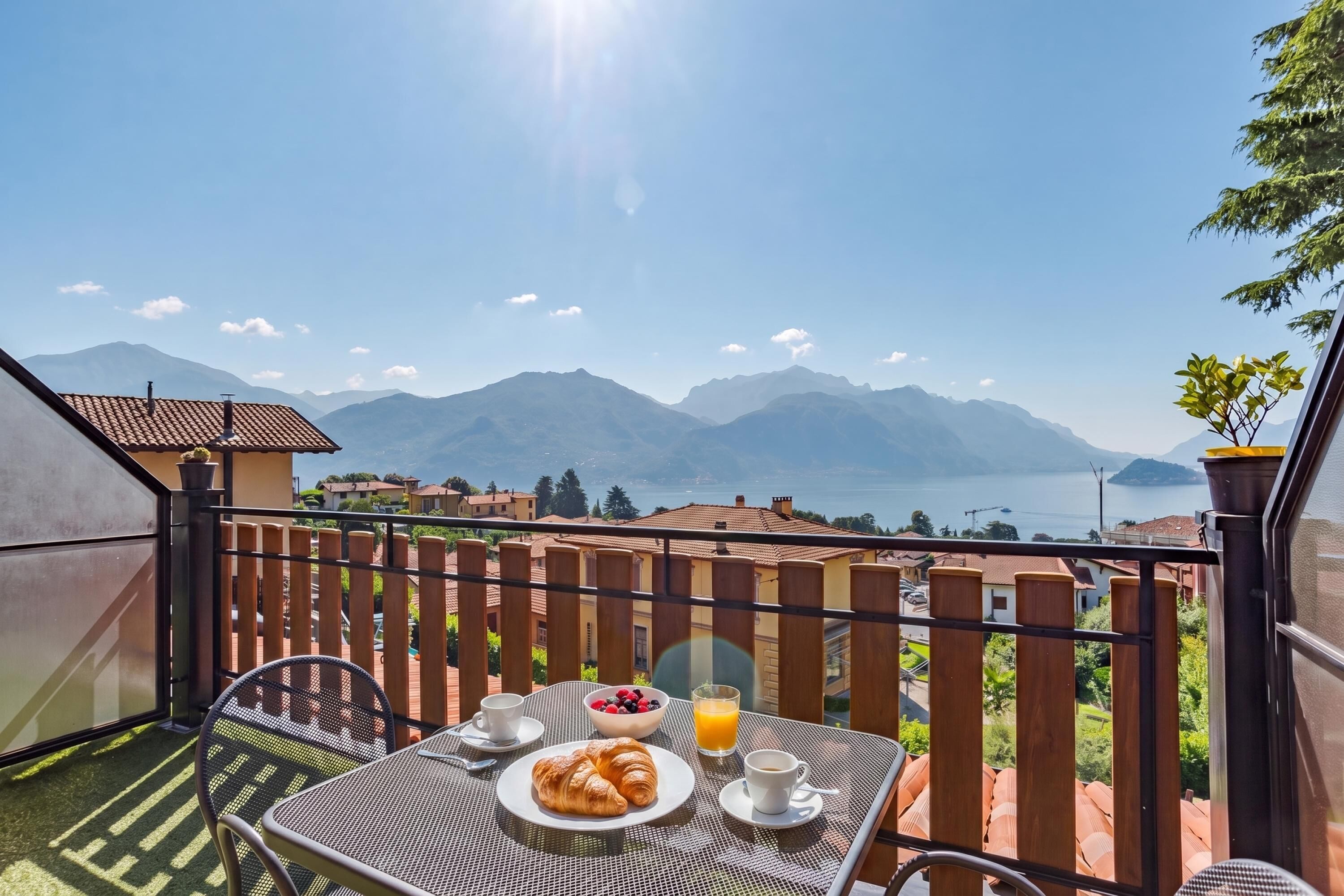 A balcony with a table set for breakfast, overlooking a mountainous landscape and a body of water.