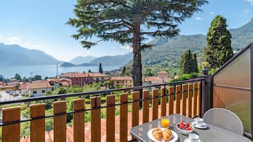 Un balcón con una mesa dispuesta para el desayuno, con vista a un lago y un paisaje montañoso.