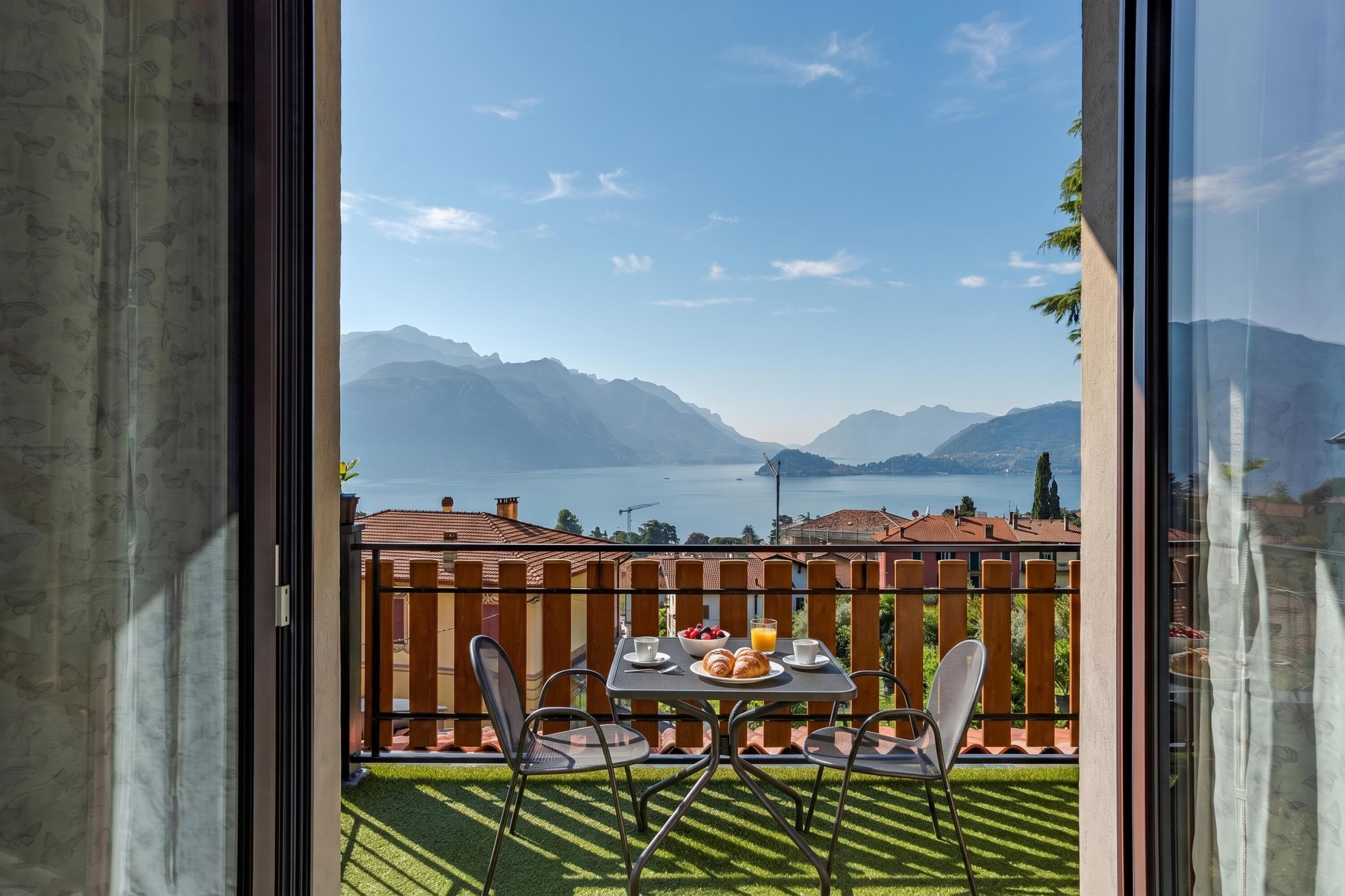 A balcony with a table set for breakfast, overlooking a lake and mountains.
