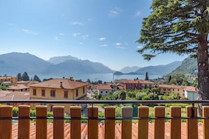 A coastal town with terracotta-roofed buildings, a clear blue sky, and a lake in the background. - Co.ri. Apartments (Menaggio)