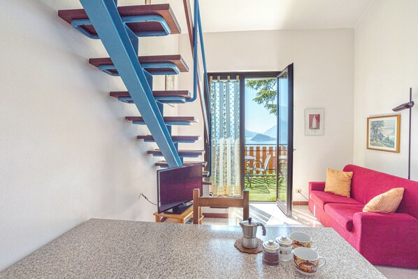 A modern living room with a staircase, a red sofa, a coffee table with cups, and a TV. - Co.ri. Apartments (Menaggio)
