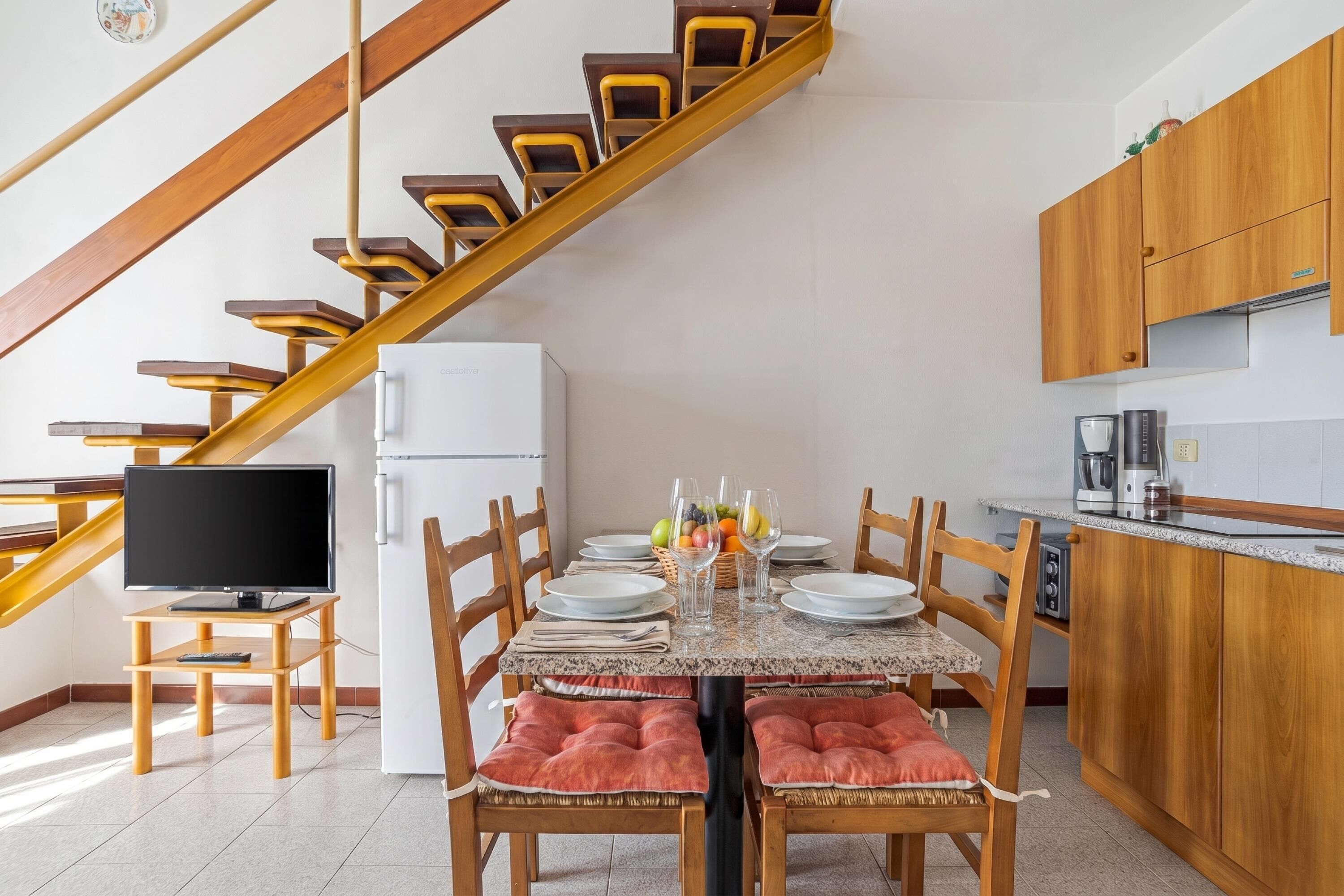 Un coin repas avec une table dressée pour quatre personnes, un téléviseur et une cuisine dotée de meubles en bois.