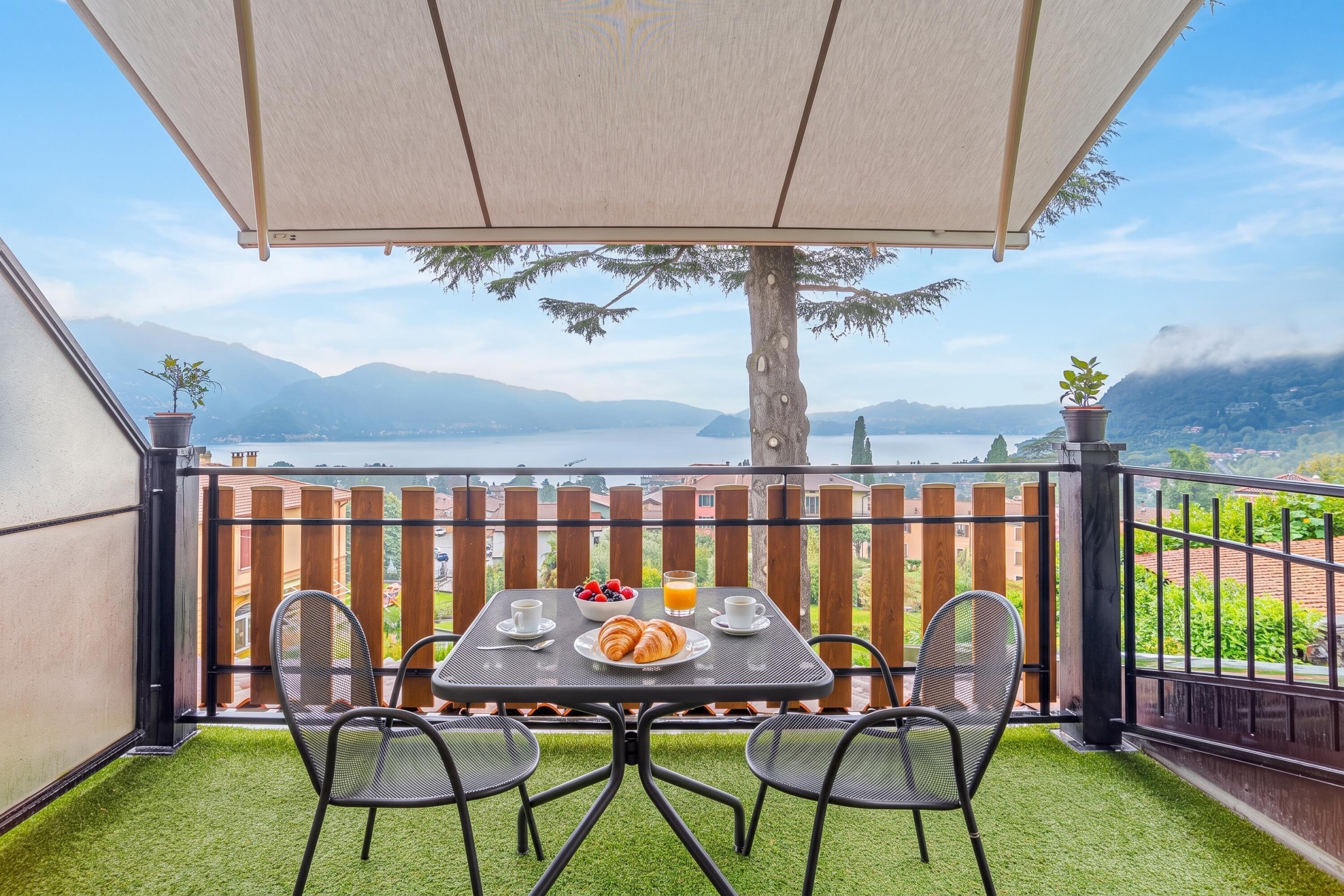 A balcony with a table set for breakfast, overlooking a lake and mountains.