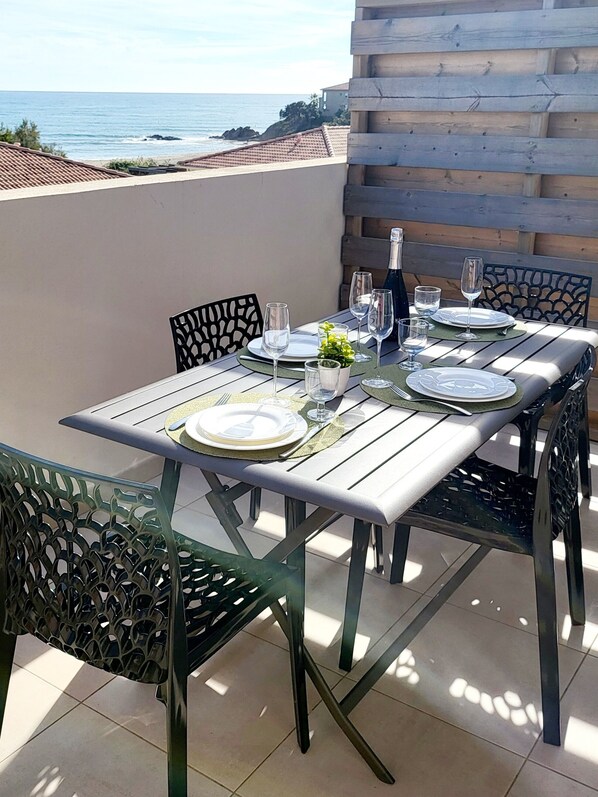An outdoor dining area with a table set for four, chairs, and a view of the ocean. - L'échappée Belle en Tout Compris (Linguizzetta)